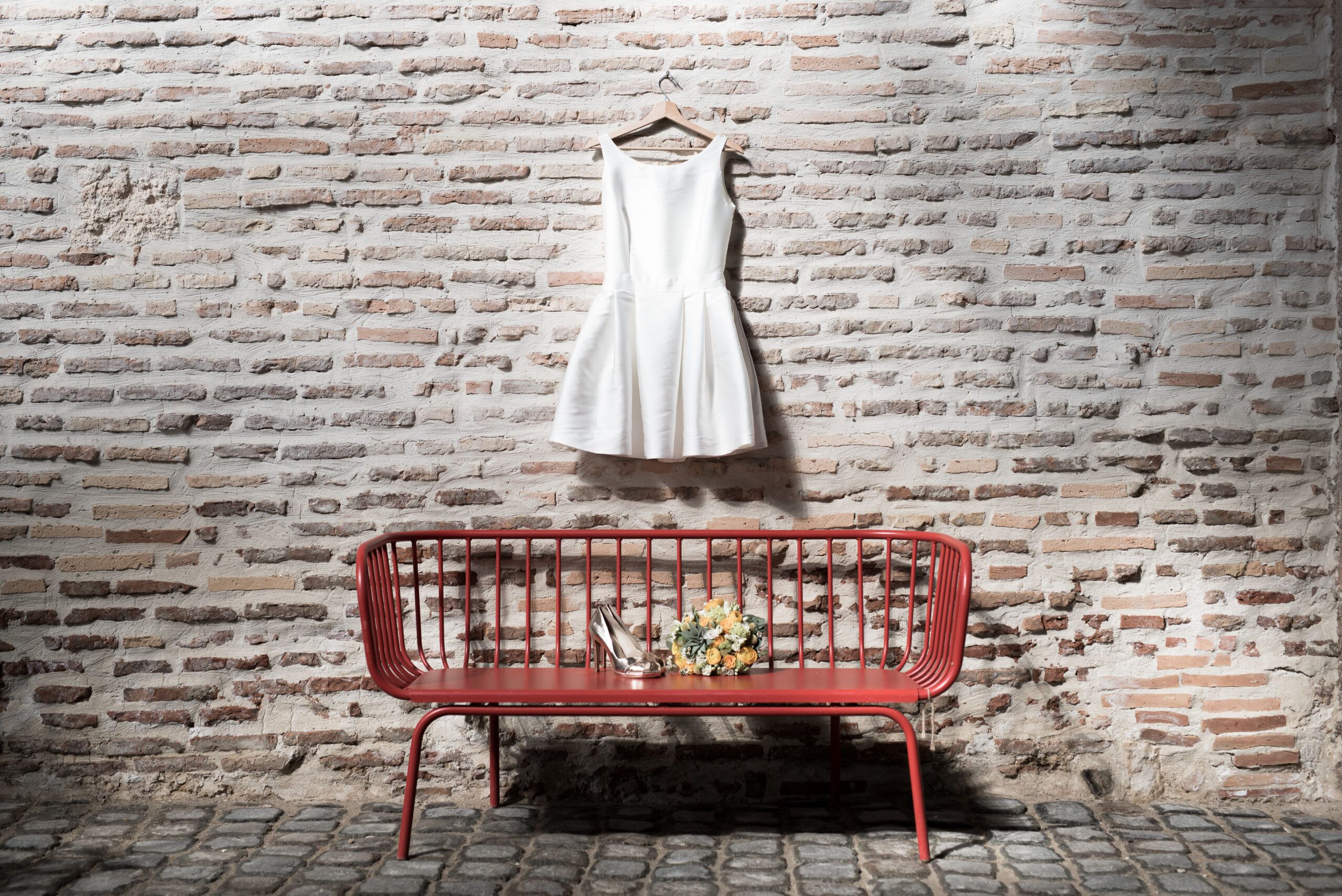 Robe de mariée courte accrochée au mur au dessus d'un banc. Organiser un mariage